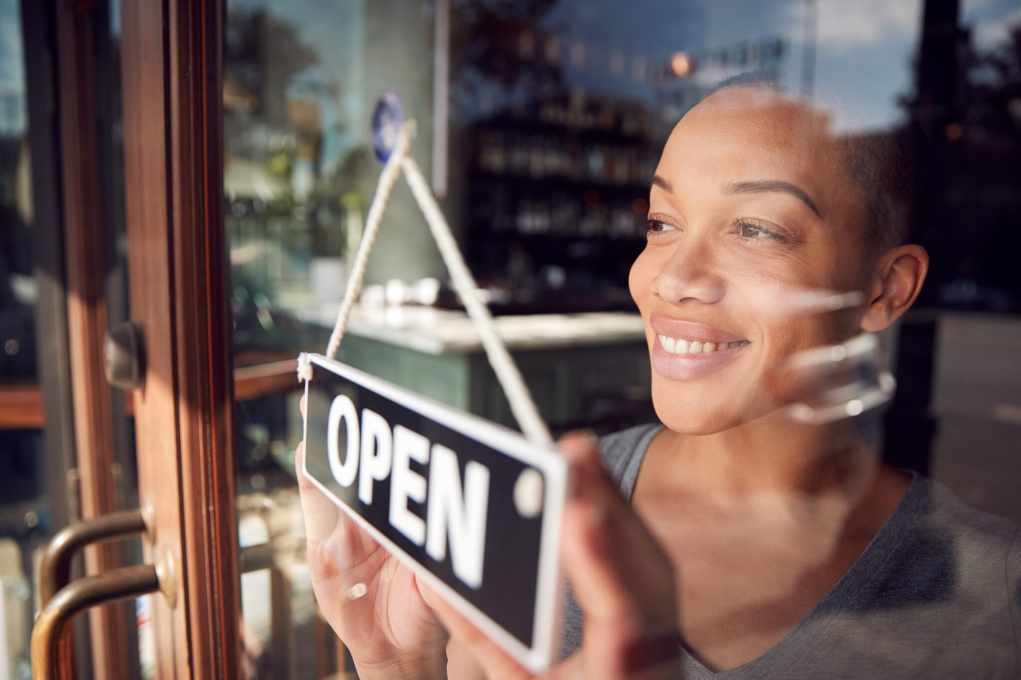 A female owner of a startup turns an “OPEN” sign on the front door of business for seasonal overflow blog.