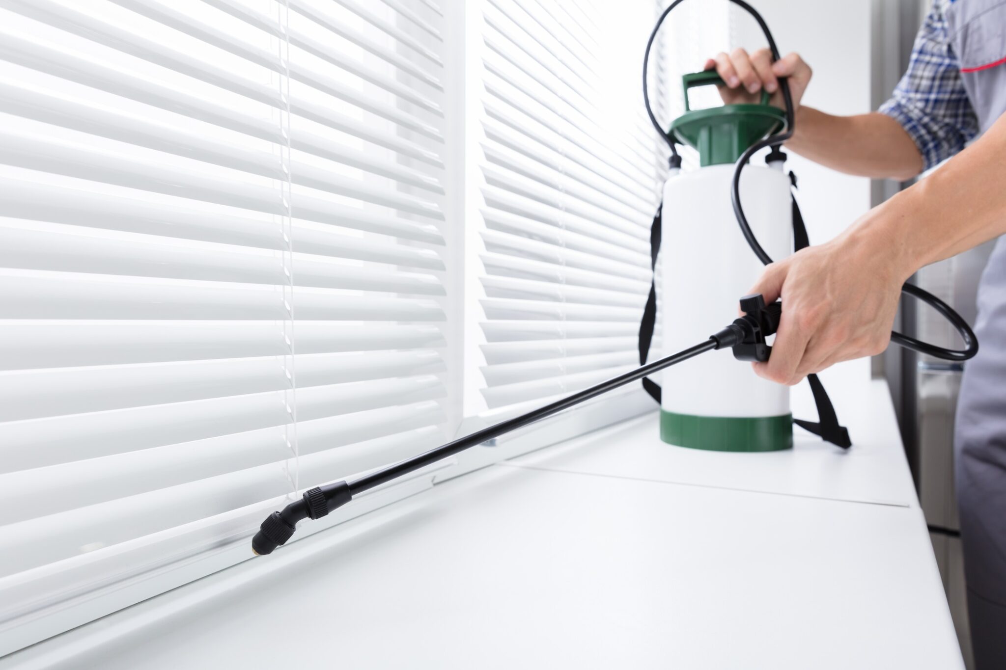 An exterminator sprays insecticide on a windowsill using sprayer for exterminator emergencies blog.