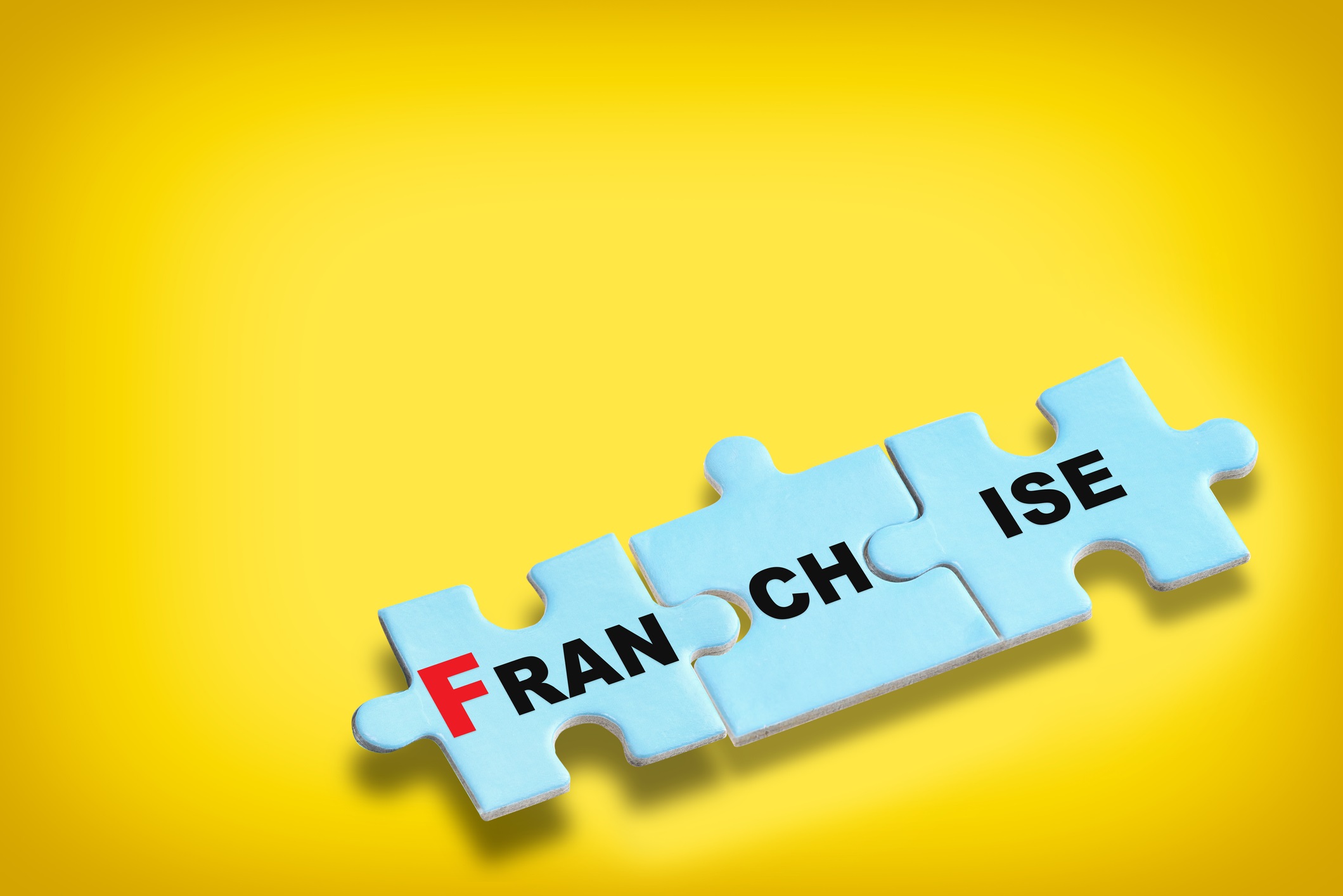 The word "franchise" is written on blue puzzle pieces set against a yellow background for fastest-growing franchises blog.