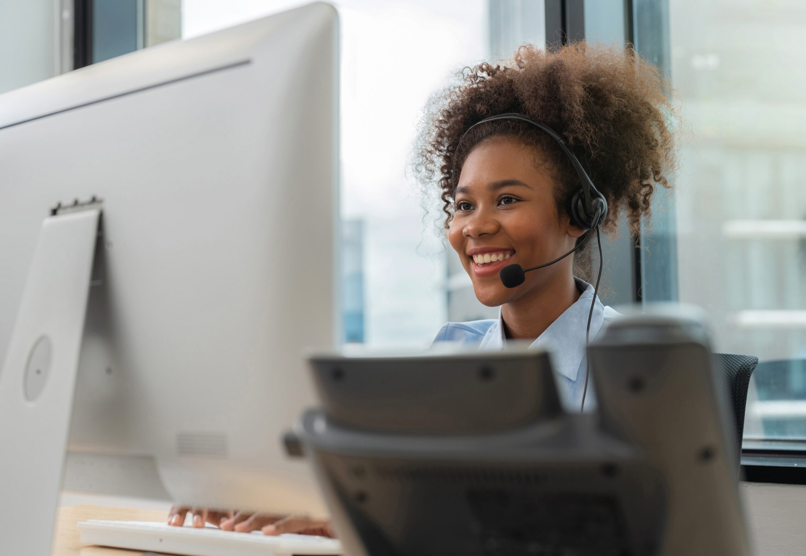 A young African American woman smiles as she talks to a customer over a headset for economic downturn blog.