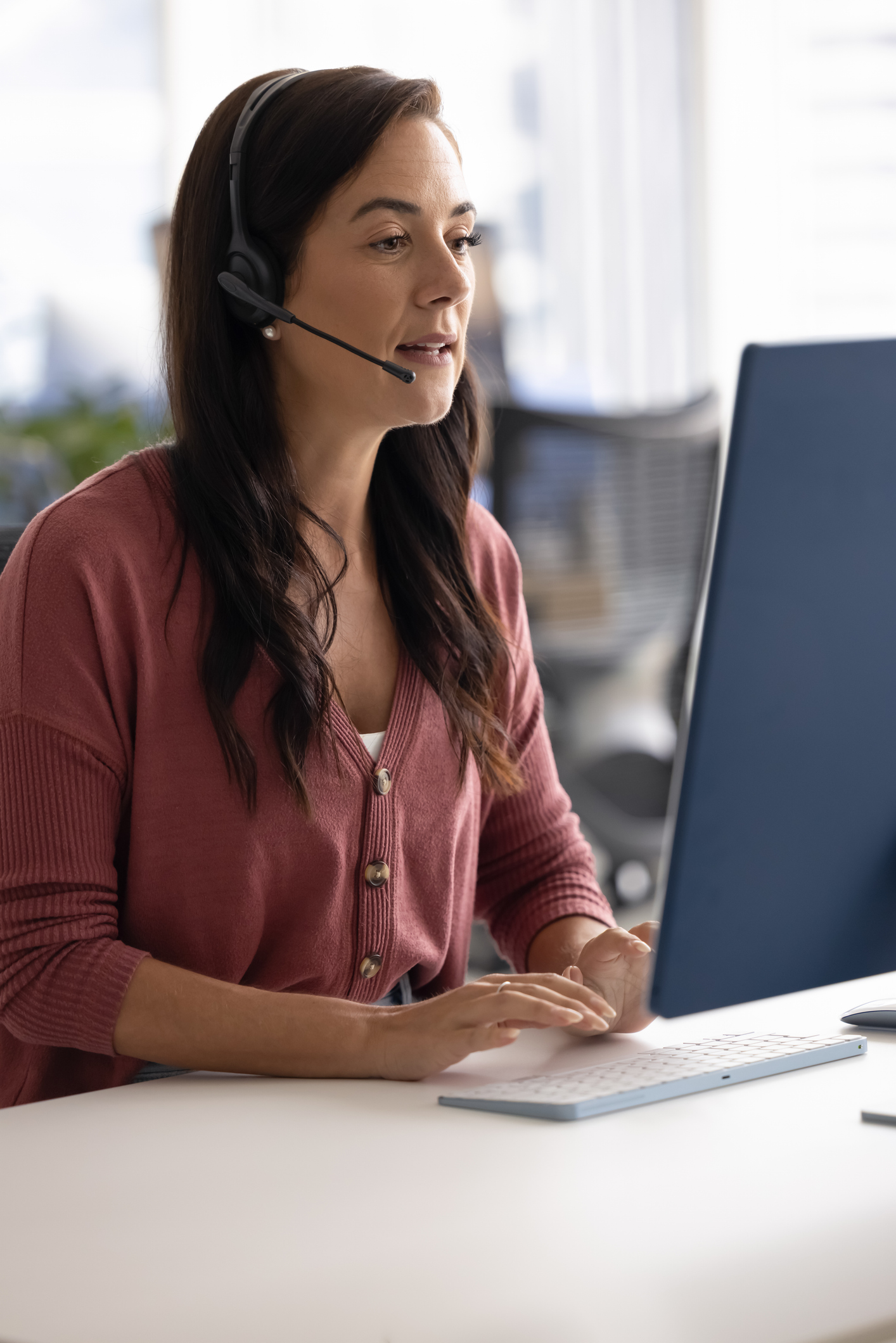 Call center. Vertical photo busy millennial female customer support manager in headset with microphone sitting before desktop computer talking to client via video call giving professional consultation