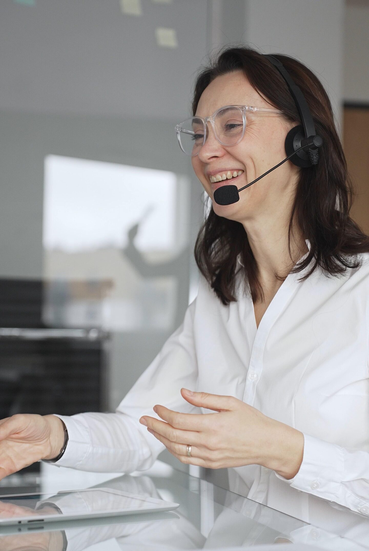 Professional woman in white blouse wearing a headset hosting a virtual conference from a modern office, using a tablet to present, gesture, and train her remote team with energy and focus