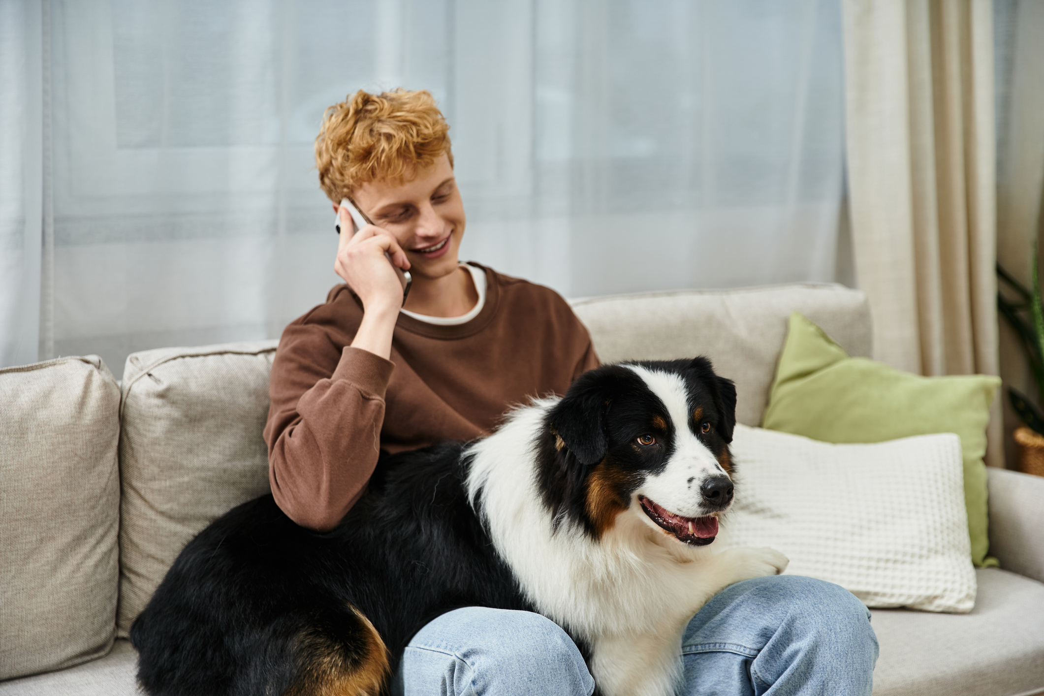 A young man with red hair chats on the phone while relaxing with his dog on the couch for Focus Answering Service
