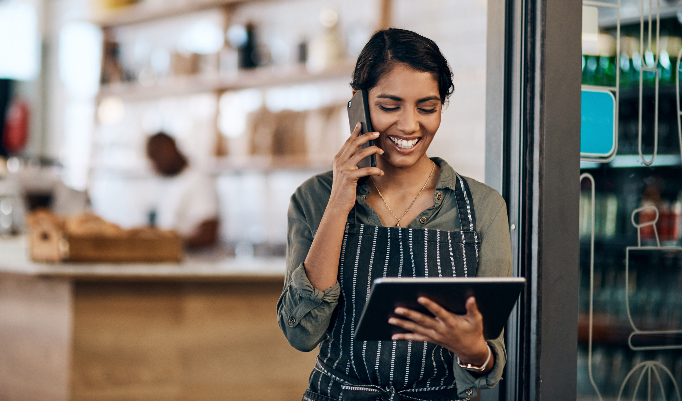 A young, female franchisee uses a digital tablet and smartphone while working in cafe for Top-New-Emerging-Franchises blog.